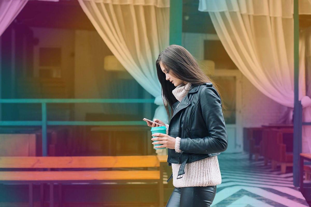 Woman walking on the street holding a coffee cup and a phone
